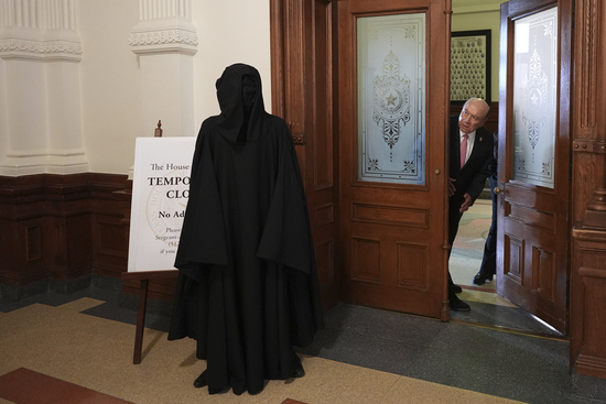 Texas state Sen. Juan "Chuy" Hinojosa, right, looks at a protester dressed as death standing outside of the House Chamber where Democratic Texas state Rep. Nicole Collier refuses to leave due to a required law enforcement escort, Tuesday, Aug. 19, 2025, in Austin, Texas. (AP Photo/Eric Gay)